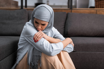 Wall Mural - sad arabian woman in hijab sitting on floor in living room, domestic violence concept