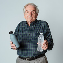 Puzzled Senior Man Holding A Reusable And A Plastic Water Bottle