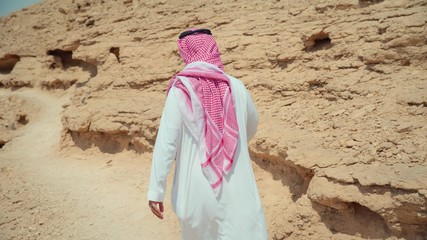 Adult man in traditional Arabian clothing walking in the desert. Saudi Arabia