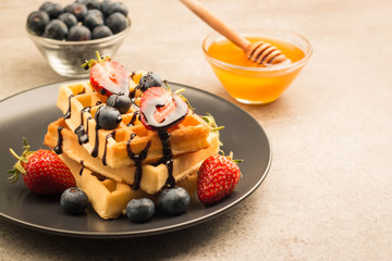 Fresh homemade food of berry Belgian waffles with honey, chocolate, strawberry, blueberry, maple syrup and cream. Healthy dessert breakfast concept with juice