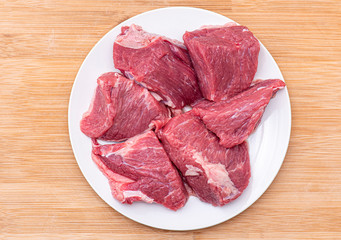 Wall Mural - Raw large pieces of beef for bbq or goulash meat on white plate, top view