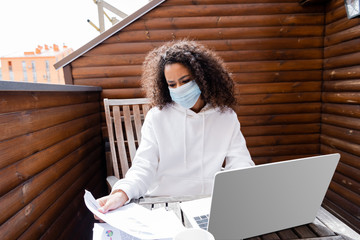 Poster - african american girl in medical mask looking at charts and graphs near laptop