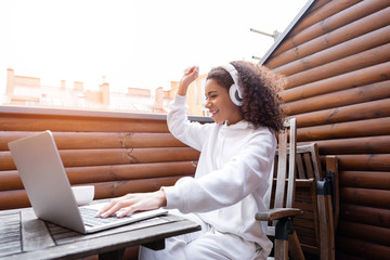 Poster - cheerful african american freelancer in wireless headphones listening music near laptop and cup of coffee