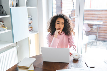 Wall Mural - african american freelancer looking at laptop near smartphone, books and cup