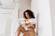 © LIGHTFIELD STUDIOS - surprised african american woman sitting on stairs with magazine