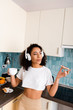 © LIGHTFIELD STUDIOS - curly african american girl in wireless headphones holding toast bread with jam and cup of coffee
