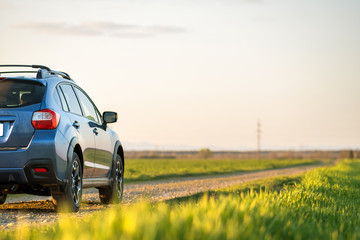 Landscape with blue off road car on gravel road. Traveling by auto, adventure in wildlife, expedition or extreme travel on a SUV automobile. Offroad 4x4 vehicle in field at sunrise.