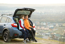 Happy couple standing together near a car with open trunk enjoying view of rural landscape nature. Man and woman leaning on family vehicle luggage compartment. Weekend travel and holidays concept.