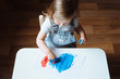 © kaloriya - Child painting with her hands on the table at home using blue and red paint. Finger painting or art therapy for children. Fun activities for toddlers. Top view.