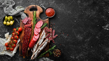 Background of salami, sausages and meat products, on black stone background. Top view. Free space for your text.