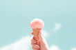 © oatawa - Hand holding strawberry ice cream cone on blue sky in summer background. Minimal style, copy space.