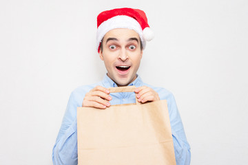 Wall Mural - Concept of a new year. Stunned guy in Santa Claus is happy to receive a gift bag, portrait, white background, copy space