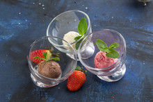 Three Scoops Of Chocolate, Strawberry And Vanilla Ice Cream In Glass Bowl On Blue Background