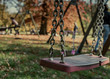 Opuszczona, samotna huśtawka w jesiennym parku na placu zabaw zawieszona na łańcuchu pośród liści