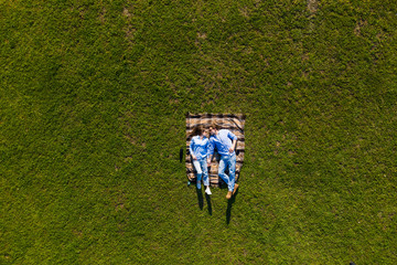 Wall Mural - Young couple lying on the grass and looking up in the park. Top view on the lying couple from above