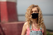 A girl with curly hair and an antiviral mask walks in sunny weather on the street

