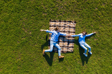 Wall Mural - Top view. Young couple sits on green grass on the field having fun while lying on blanket