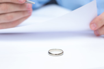 Husband signing decree of divorce, man's hands, closeup. Wedding ring in the foreground