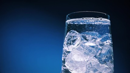 Wall Mural - pouring water into glass close-up, water with ice cubes isolated on dark blue background with copy s