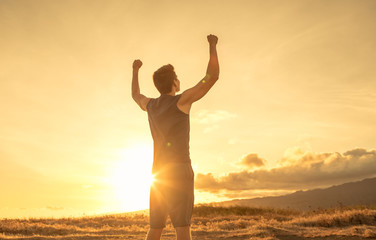 Wall Mural - Young man flexing his arms on a mountain top. People feeling strong and confident, and never giving up concept. 