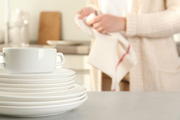 Poster - Woman wiping plate with towel in kitchen, focus on stack of clean dishes