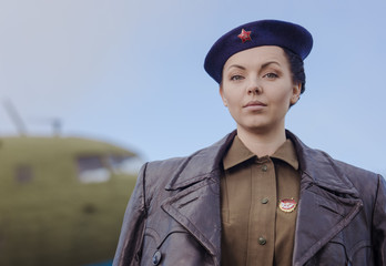 A young female pilot in uniform of Soviet Army pilots during the World War II. Military shirt with shoulder straps of a major and a beret. Against the background of a military aircraft.