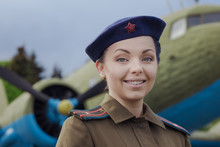 A Young Female Pilot In Uniform Of Soviet Army Pilots During The World War II. Military Shirt With Shoulder Straps Of A Major And A Beret. Against The Background Of A Military Aircraft.