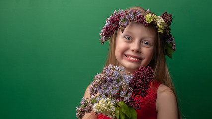 A beautiful flowering girl in a lilac wreath with white skin with a bun rejoices with bright daylight. Make up, grimace