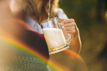 Wall Mural - Close-up of the girls hands in dirndl pouring a full glass of beer with huge foam outdoors