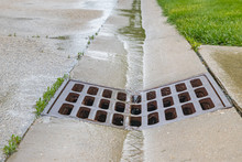 Closeup Of Rain Water Running Down Street Gutter And Flowing Into Storm Sewer System Drainage Grate