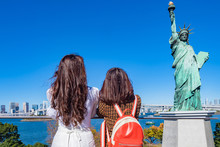 Japan. Statue Of Liberty On Odaiba Island. Two Girls Look At The Statue Of Liberty In Tokyo. Attractions Of The Japanese Capital. Women And A Statue Against The Blue Sky. Monuments Of Tokyo.