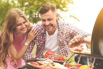 Canvas Print - Young couple having barbecue with modern grill outdoors