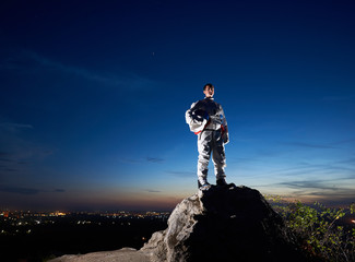 brave astronaut standing on top of rocky hill with beautiful blue sky on background. handsome spacem