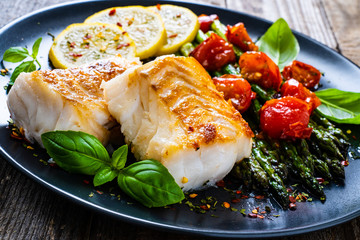fish dish - fried cod fillet with asparagus on wooden table