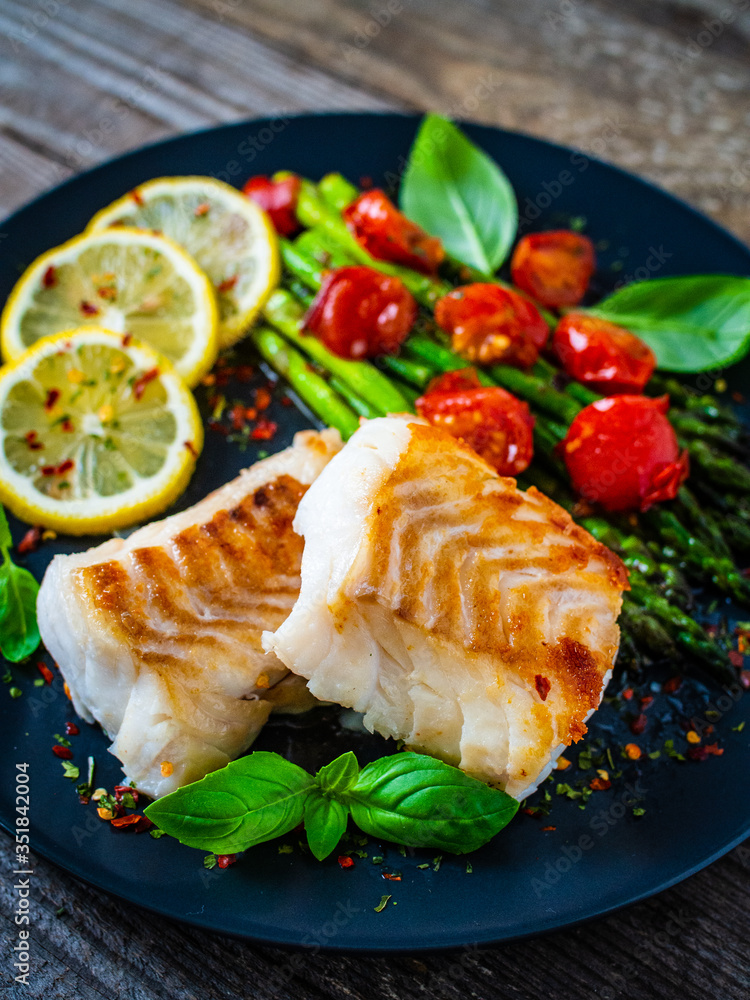Fish dish - fried cod fillet with asparagus on wooden table
 - obrazy, fototapety, plakaty 