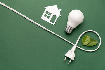 Flat lay top view of white paper house, LED light bulb, plug-like and fresh leaves on green background with copy space. Save energy concept. Minimal style