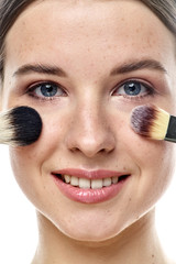 close-up portrait of a young brunette girl with blue eyes with clear skin, doing makeup with makeup brushes, isolated on a white background. High-resolution photos