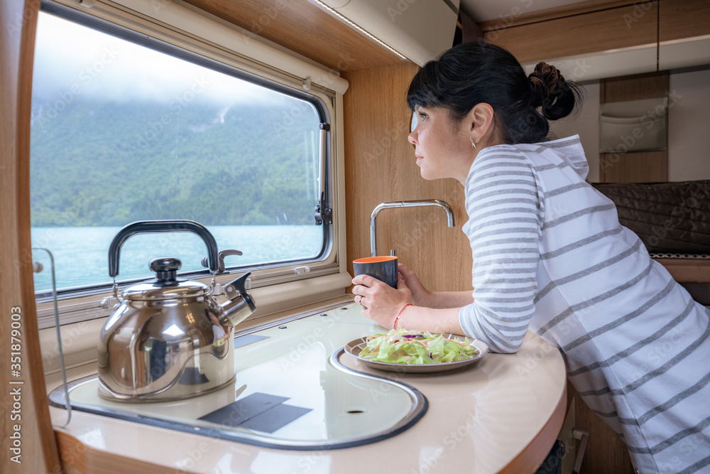 Woman in the interior of a camper RV motorhome with a cup of coffee looking at nature. - obrazy, fototapety, plakaty 