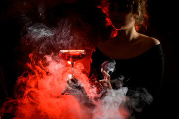 Young woman carefully holds glass with bright cocktail in front of her.