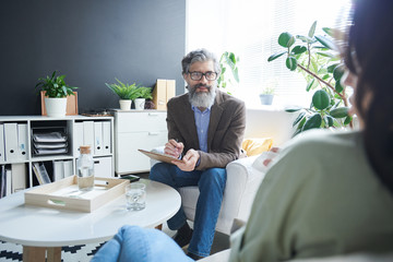 Wall Mural - Friendly senior psychologist in formalwear looking at young worried female