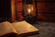© HAMERCAT - Reading a book in the light of an old hand-held kerosene lamp glows softly in a dark room on the table. Vintage style. The light in the darkness. Atmospheric photo in the loft style.
