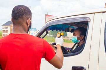 Wall Mural - young black man wearing a nose mask, checking the temperature of a black woman driving a car