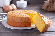 Homemade Round Sponge Cake Or Chiffon Cake On White Plate So Soft And Delicious With Ingredients: Eggs, Flour, Milk On Wood Table