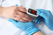 Doctor examining patient with modern fingertip pulse oximeter in bed, closeup