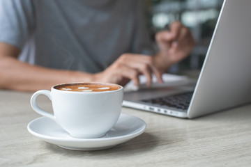 Wall Mural - Casual business man surfing the internet while online working on laptop computer with cup of coffee on table in coffee shop