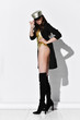 © Dmitry Lobanov - Young beautiful brunette woman in golden swimsuit, cap, black high boots and jacket standing over white wall full body