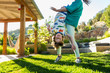 © Marc Romanelli - teenager sister holding her younger brother upside down on green lawn at sunset