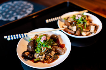 Traditional japanese house or ryokan restaurant with black lacquered wood table and food dish closeup of oden tofu mushrooms topped with pickled sakura flower