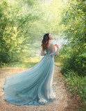 fairy tale princess in light summer blue, turquoise dress standing in park. Happy Woman walks towards wind, graceful dancing girl goddess in image of flower. flying long hem of dress. nymph of forest