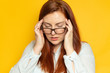 © Shi  - Having a headache concept. Tired woman in a blouse and eyesight glasses with stress on a yellow wall background. Hold hands on head